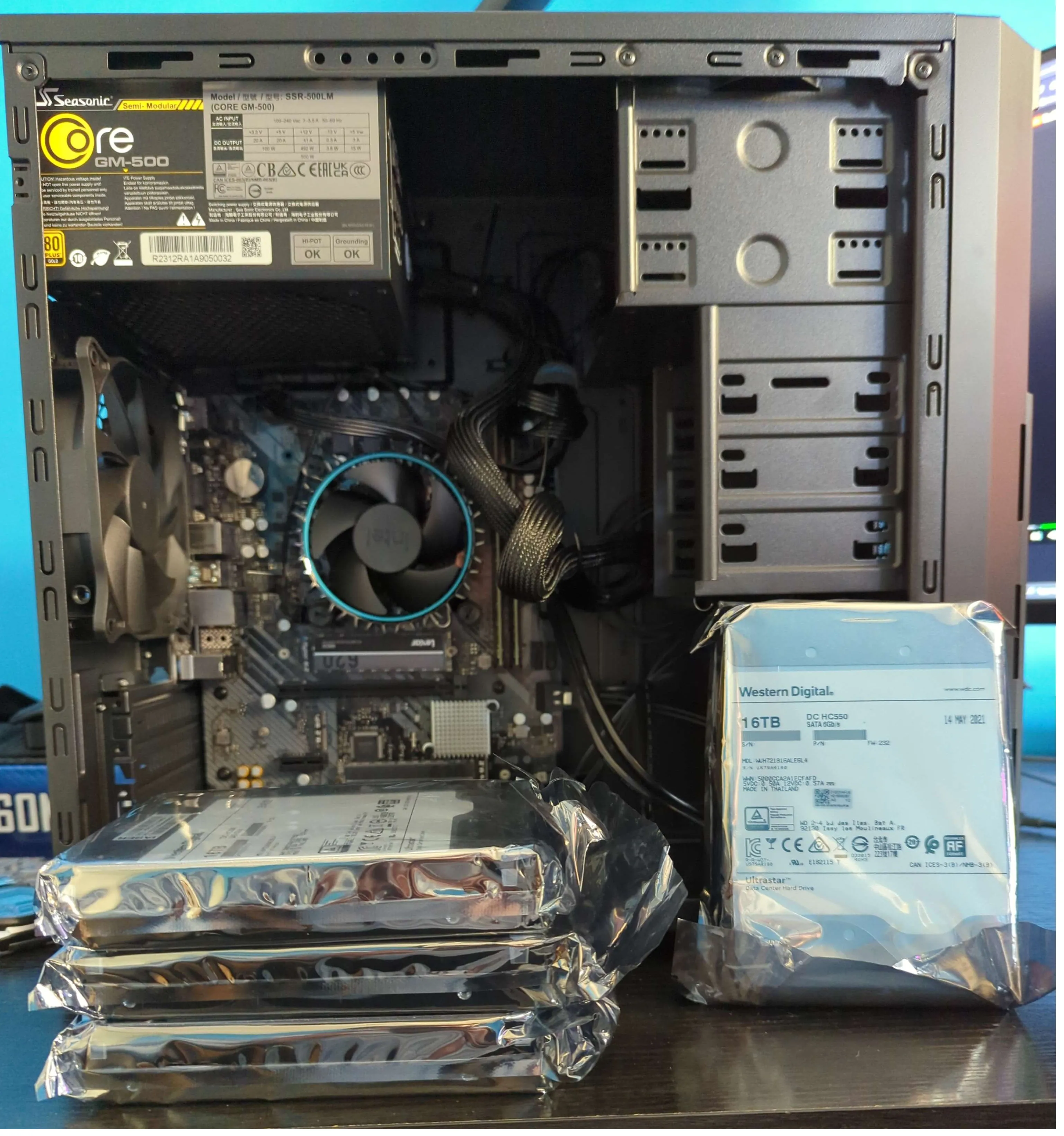 An assembled desktop computer with the side panel removed, with packaged hard drive disks leaning on the case